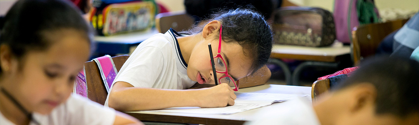 Criança escrevendo em carteira na sala de aula
