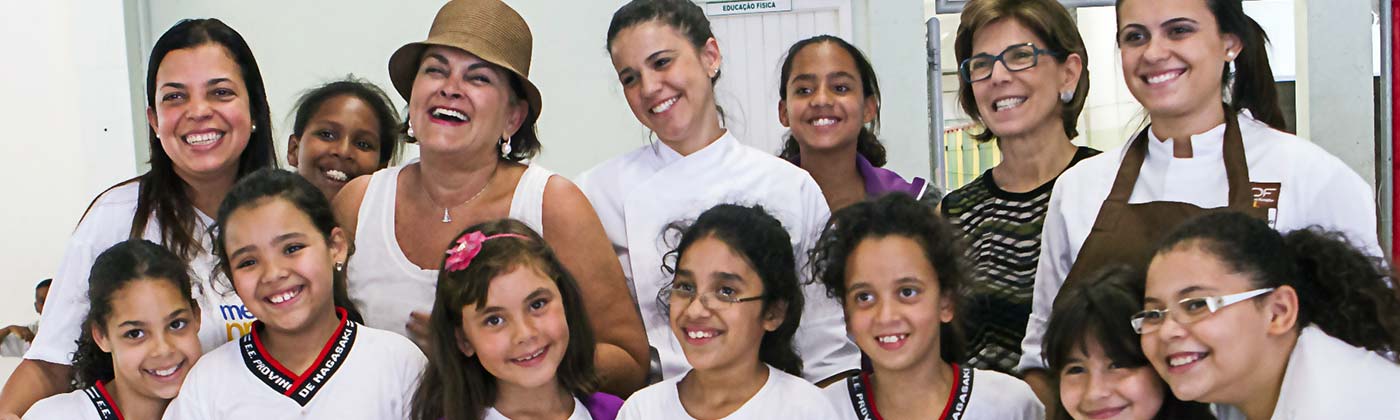 Imagem mostra profisionais e alunos da Educação pública de São Paulo juntos dentro de uma escola e sorrindo para a foto