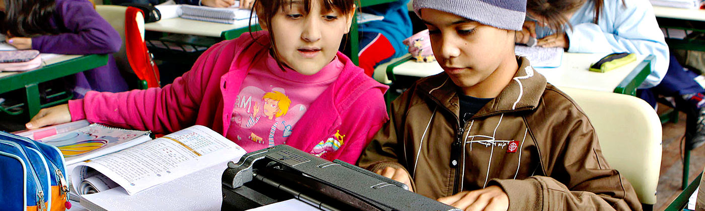 Crianças dentro de uma sala de aula interagindo com uma máquina de datilografia em Braille
